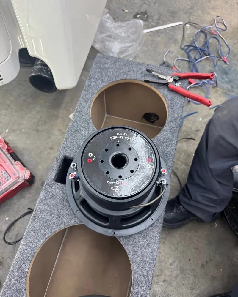 A subwoofer out of its enclosure on the shop floor during an install at Mr. Tint, tools beside it