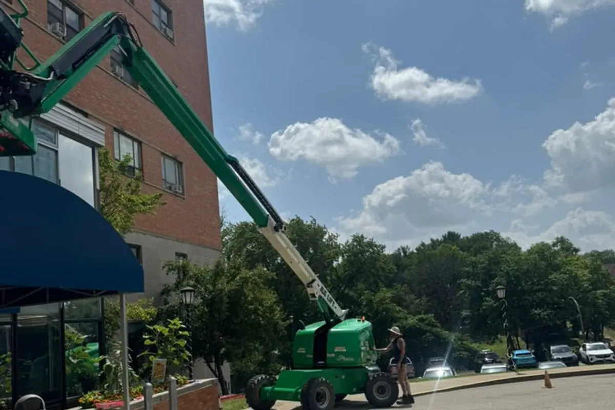 A boom lift raised to the upper floors of a multi-storey brick building while Mr. Tint fits window film