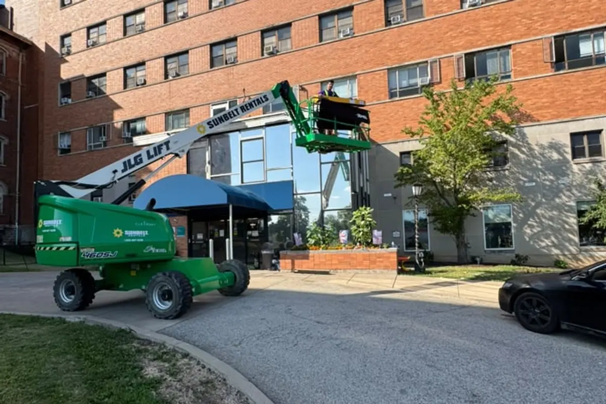 A boom lift beside a brick building with a blue awning, positioned for window film work above the entrance