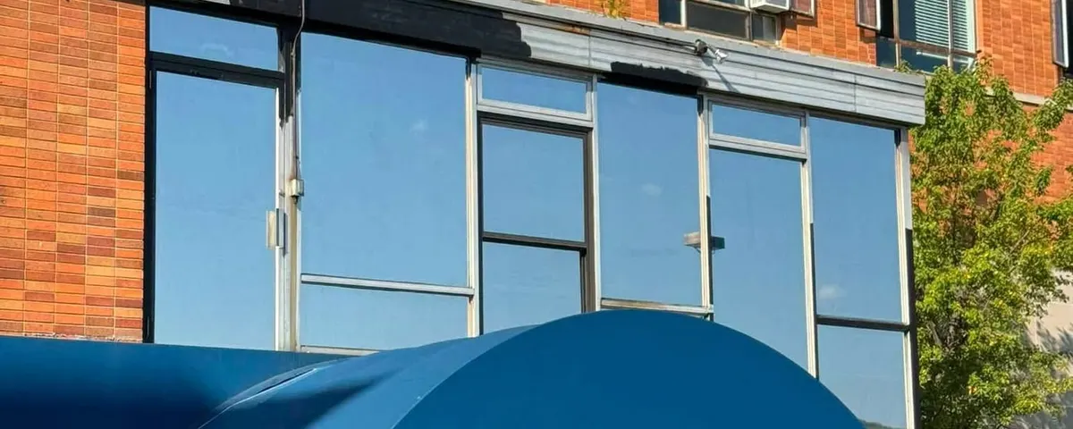 Solar control film on the first-floor glazing of a Pittsburgh commercial frontage, above a blue awning
