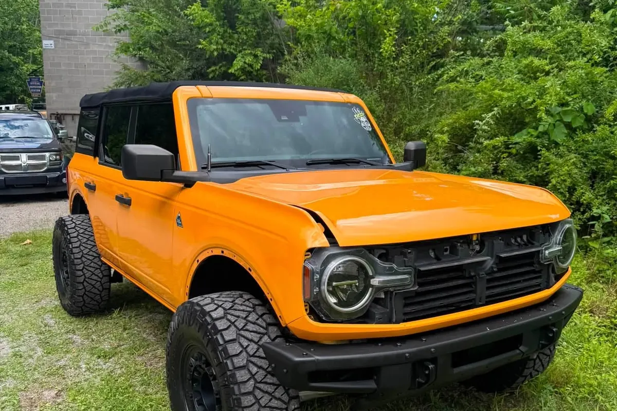 A Ford Bronco in an orange and white wrap parked on grass