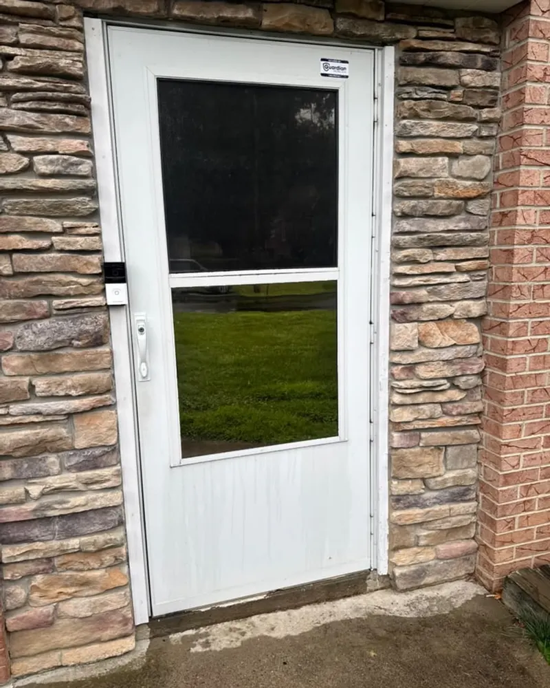 A white glazed door in a stone-clad wall, looking out onto a lawn