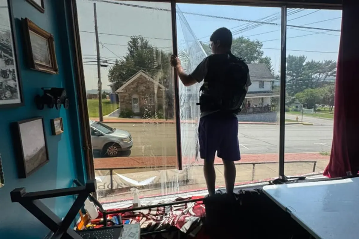 A Mr. Tint installer applying window film to a large window from inside, with a street visible through the glass