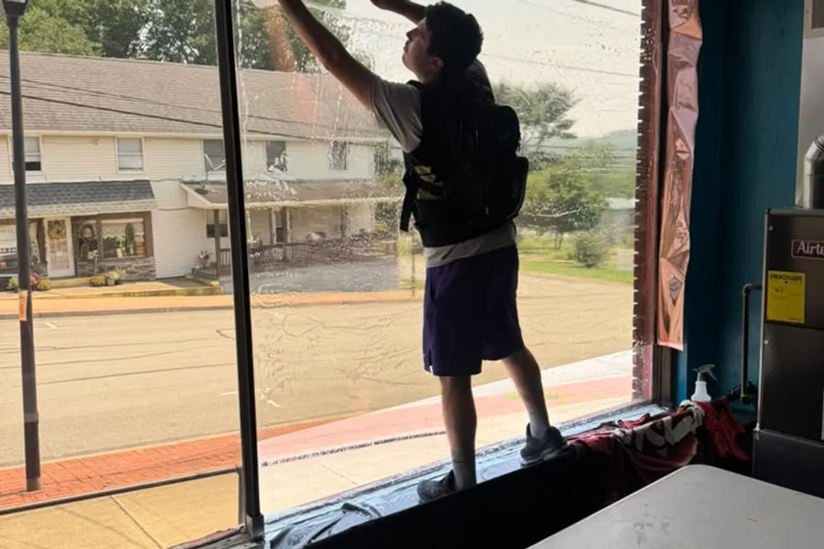 A Mr. Tint installer reaching up to smooth window film across the top of a tall window