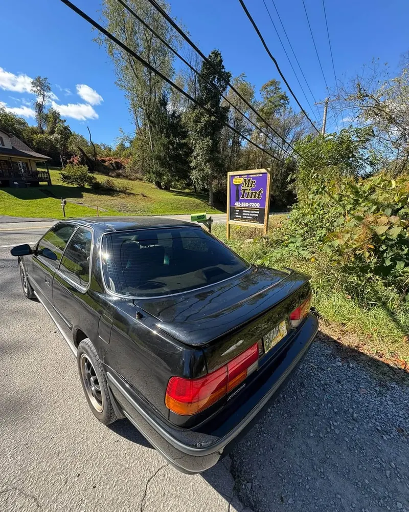 The Mr. Tint road sign in Plum, Pennsylvania, with a car parked beside it