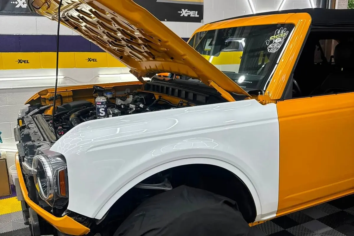 A Ford Bronco in an orange and white wrap inside the Mr. Tint bay